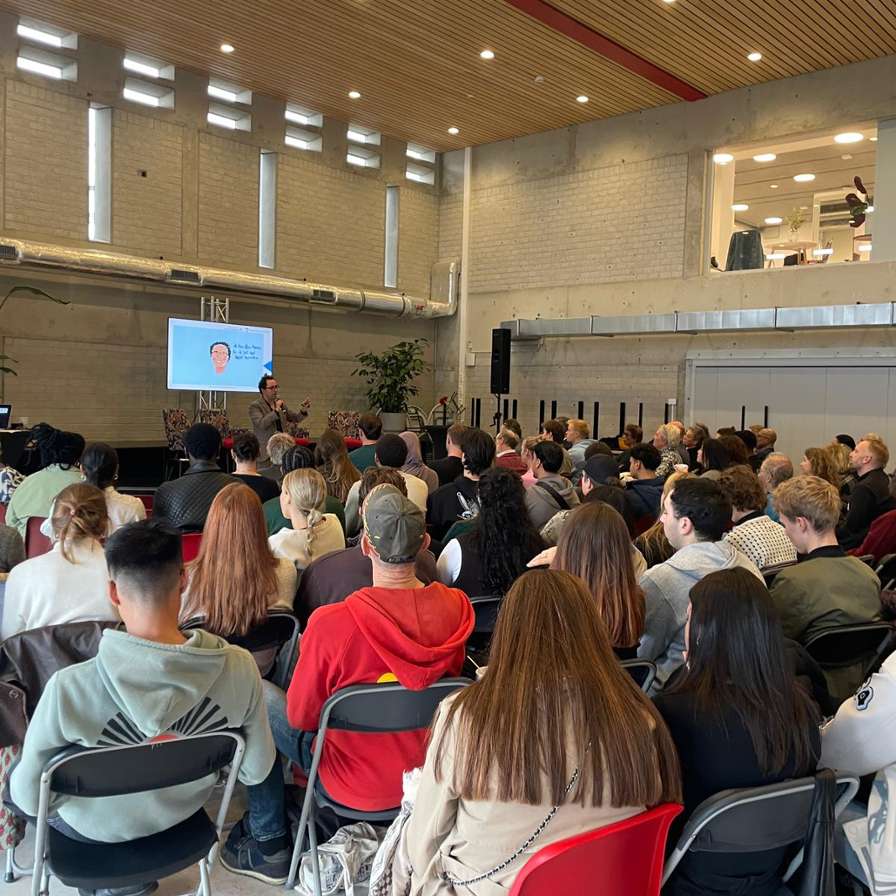 Een zaal vol mensen op klapstoeltjes tijdens het evenement Just.City.Amsterdam.2025 in Amsterdam Zuidoost
