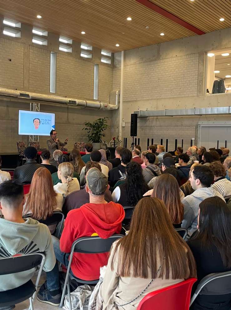Een zaal vol mensen op klapstoeltjes tijdens het evenement Just.City.Amsterdam.2025 in Amsterdam Zuidoost