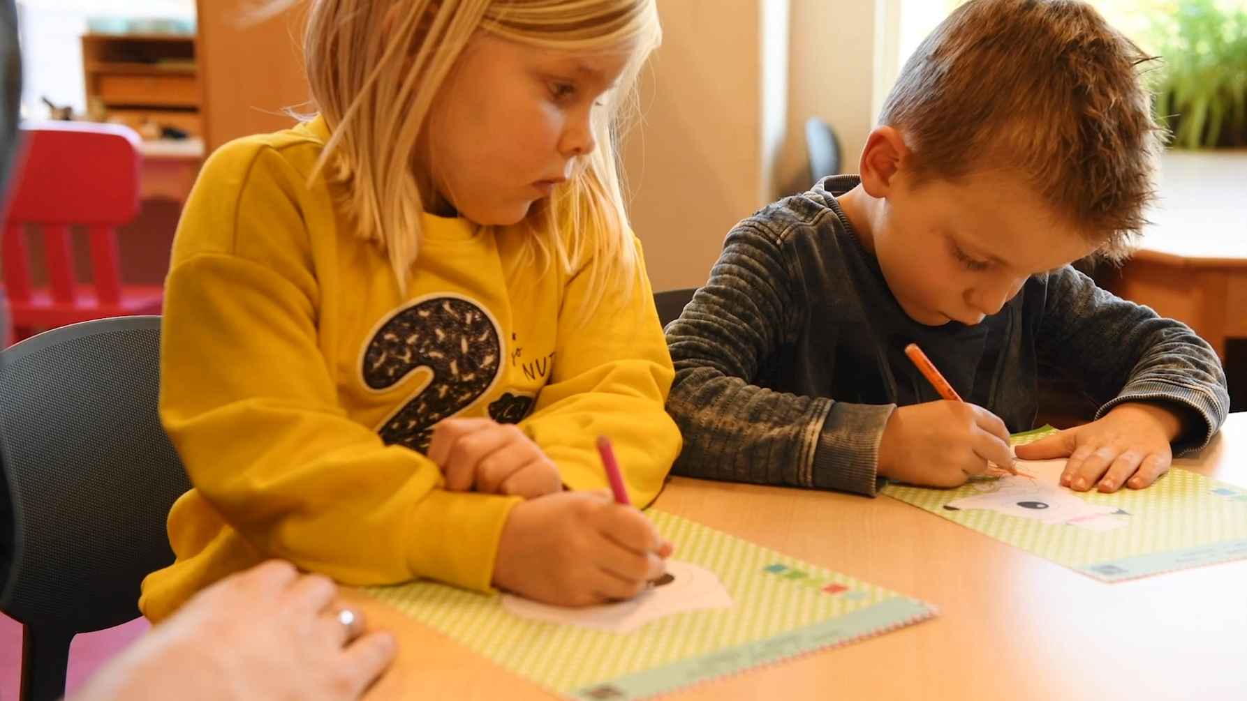 twee kleuters (meisje en jongen) zitten aan tafel te tekenen op papier