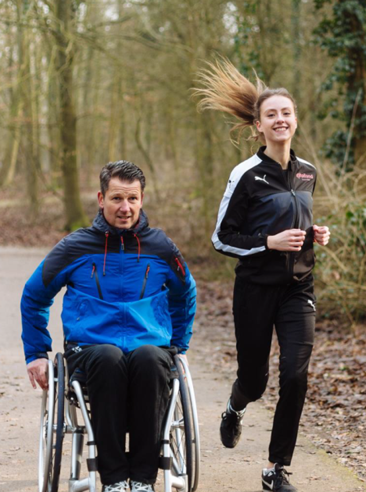 man in rolstoel in bos met hardloopster ernaast