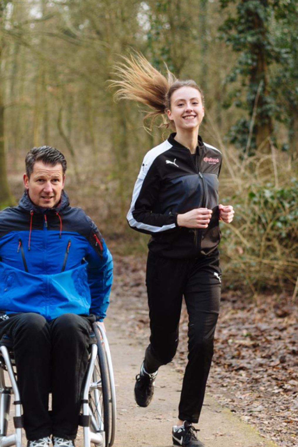 man in rolstoel in bos met hardloopster ernaast