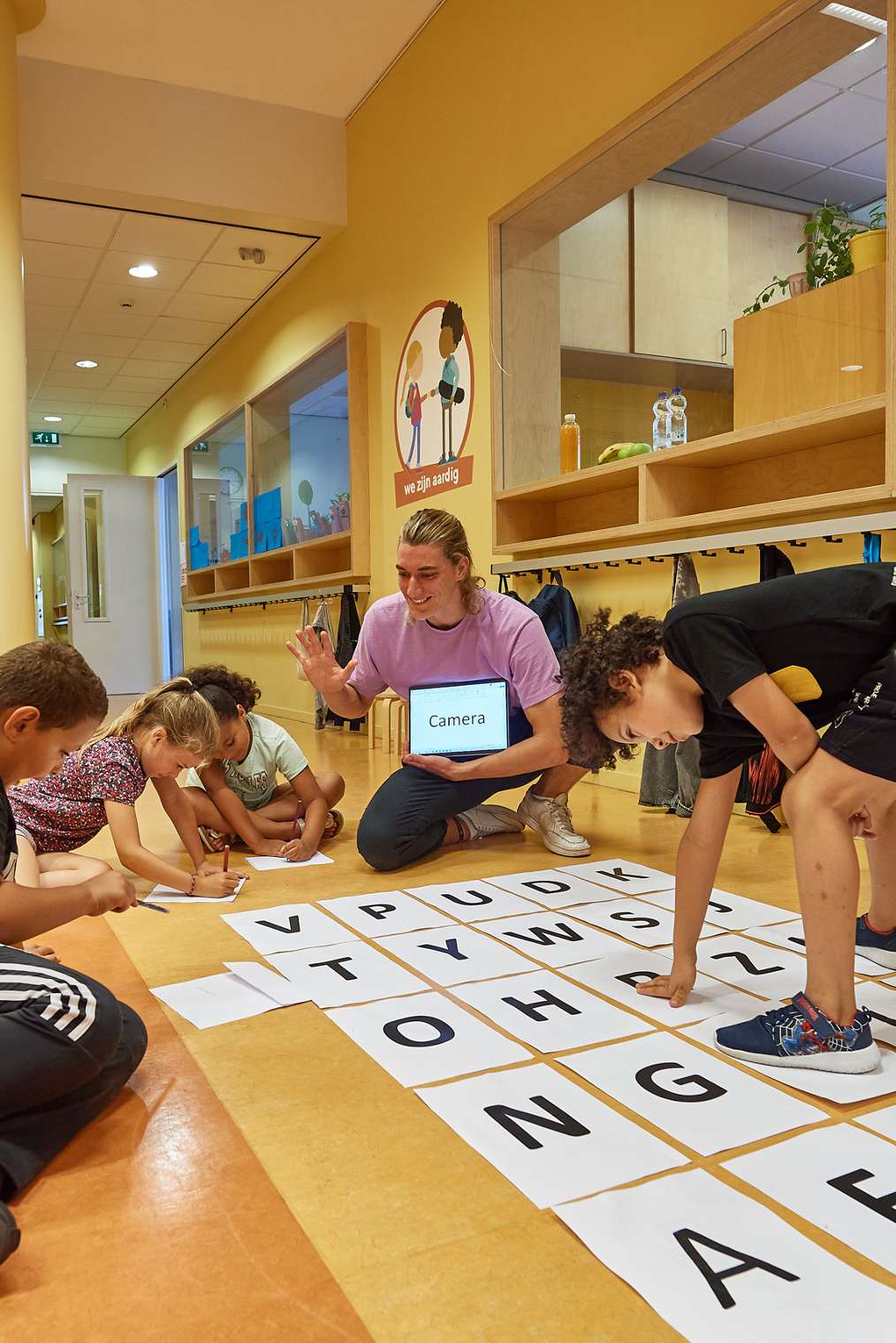 leerlingen werken op de grond in hal van school aan spellingopdracht met de leerkracht, pabo-alo HvA