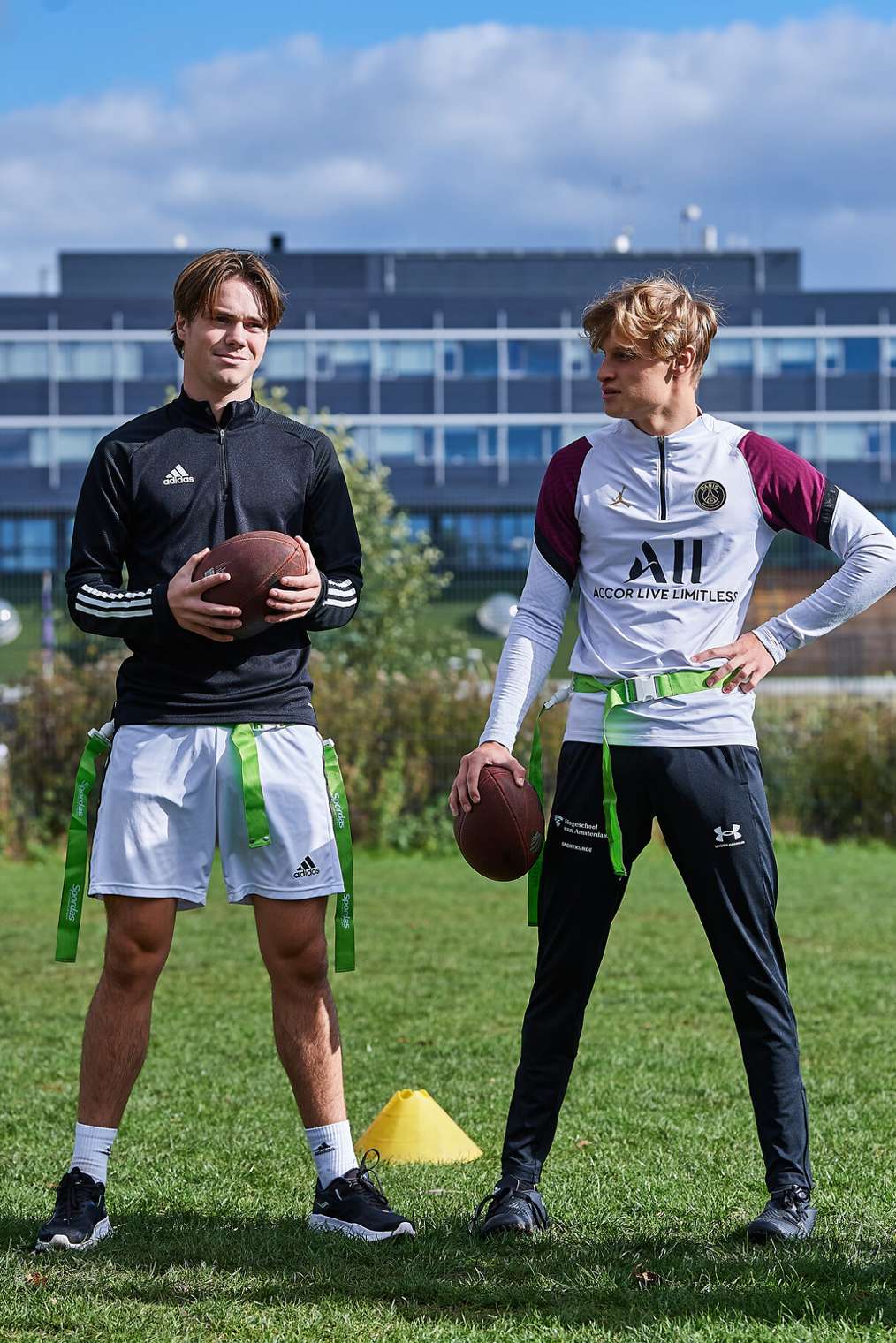 twee Sportkunde studenten staan op grasveld met rugbybal in hun hand