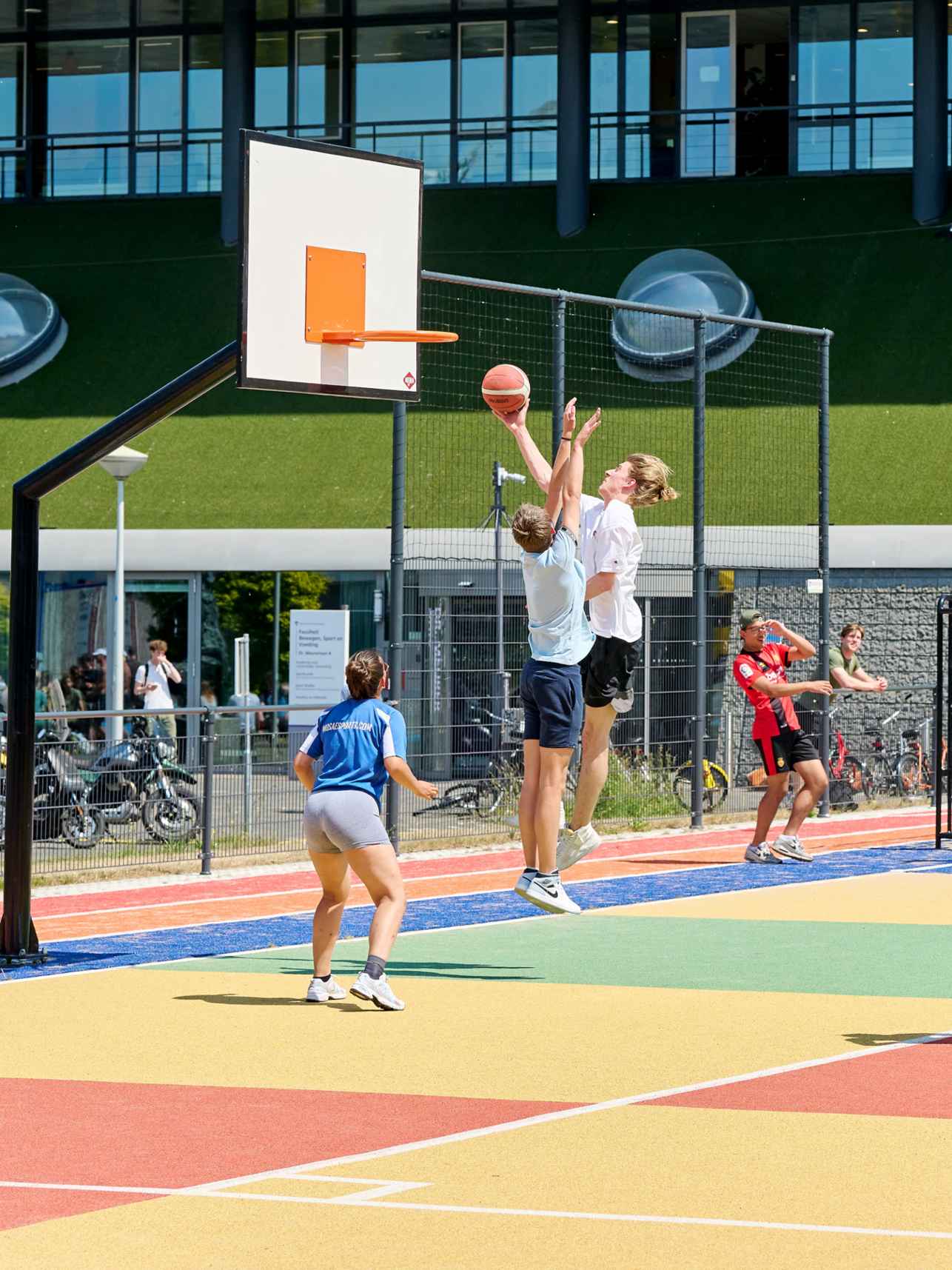 Studenten spelen basketbal buiten op plein ALO